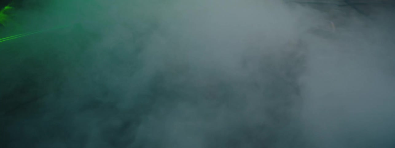 The fog rolls over the man on the ground with a green laser passing by