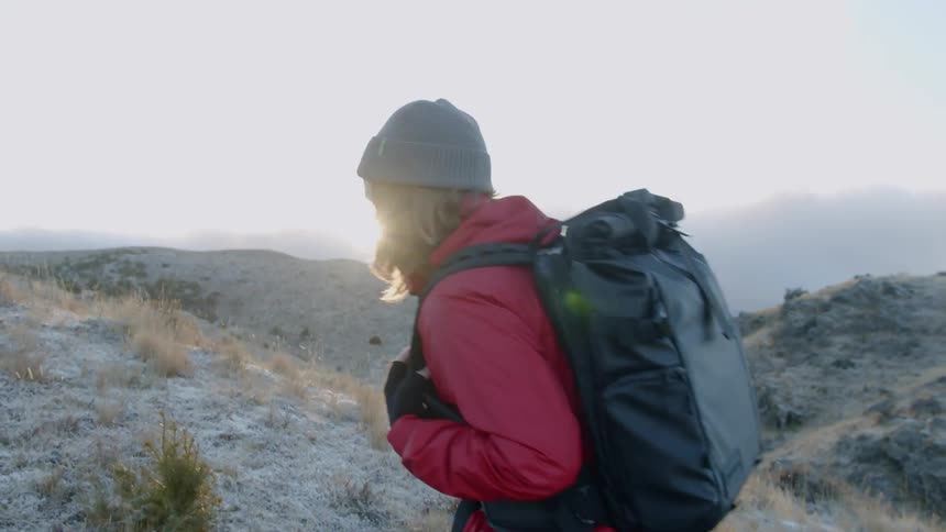 A woman wearing a backpack hikes up a snowy and icy hill on a sunny day