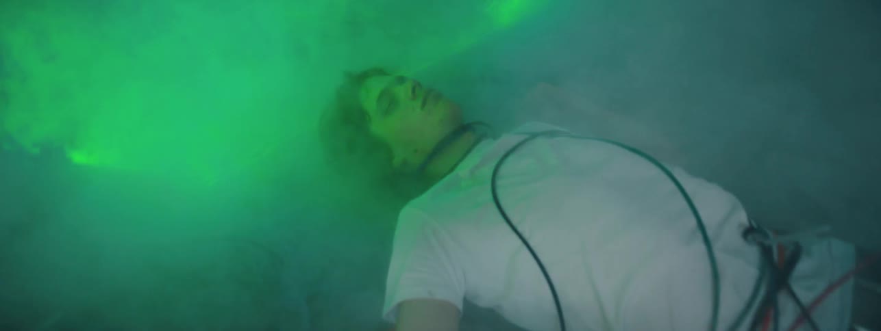 The green strobe light shines over the man laying in the fog