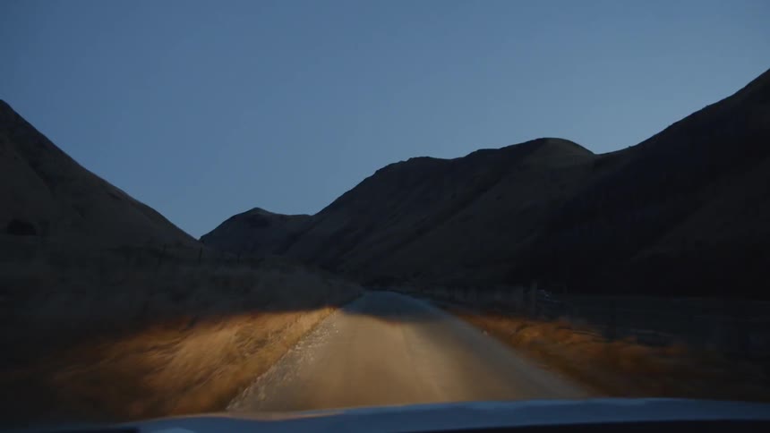 Headlights stream along a rural road at dusk