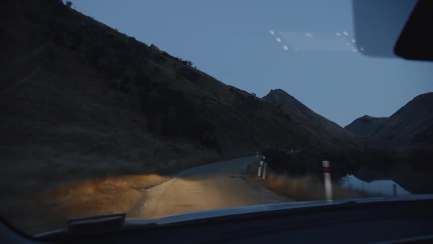 A car's lights are shining on the road ahead as it drives at dusk