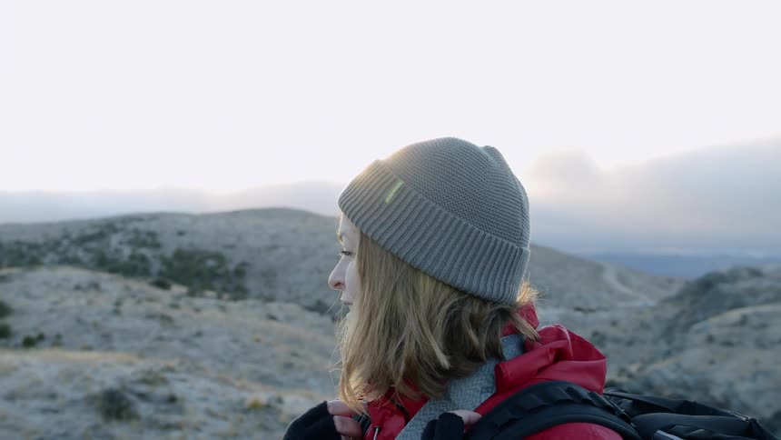 The woman smiles looking around the top of a mountain