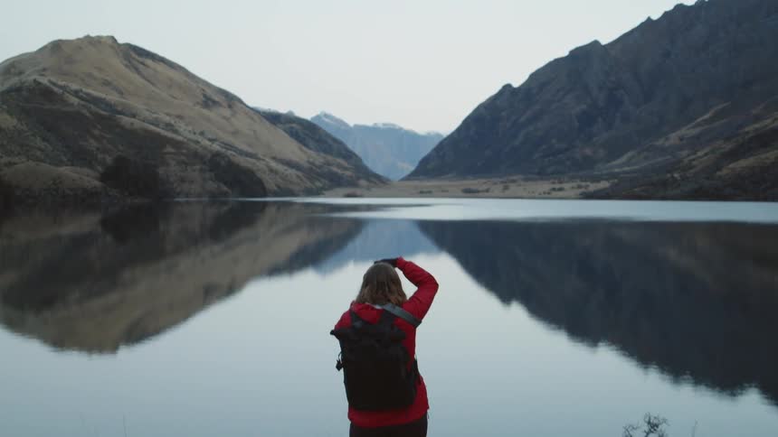A woman takes a picture of a lake surrounded by mountains
