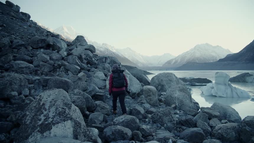 Woman walking around rocks and climbing a hill next to a river