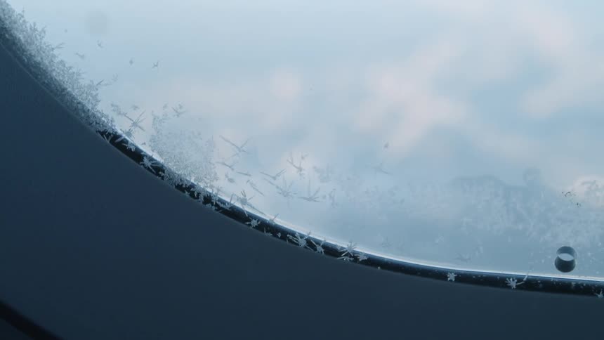 Ice crystals sit on the round window under a blue sky