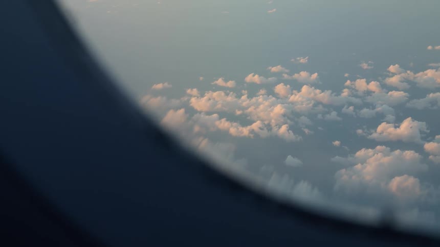 Clouds are floating in the sky outside an airplane window in daylight