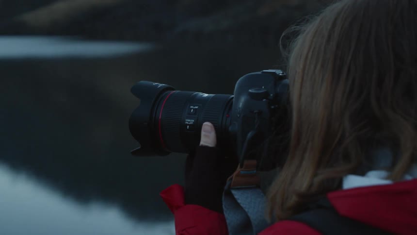 A woman is taking photos of a lake with an slr camera in daylight