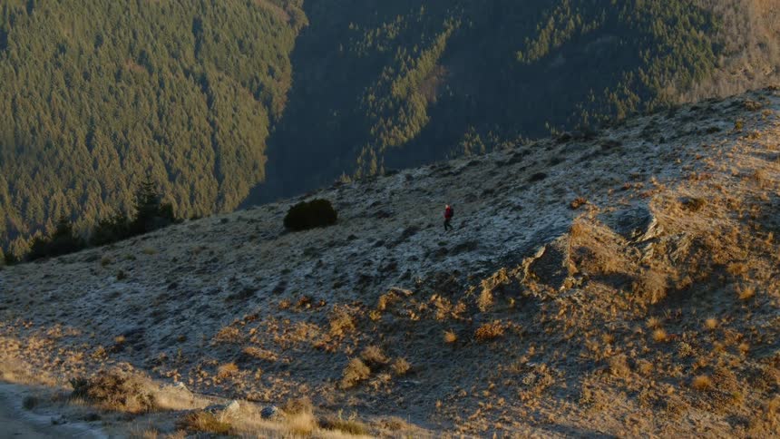 A hiker wearing a backpack is descending a mountainside in late afternoon