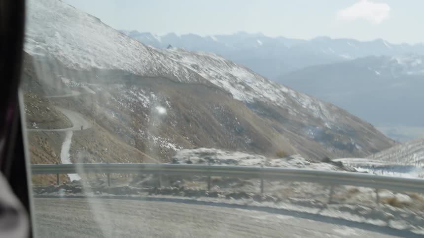 A vehicle travels down a cliff side road during winter