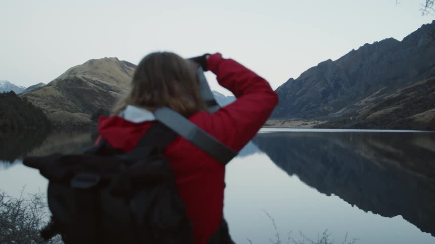 Woman taking a picture of a mountain range surrounding a lake