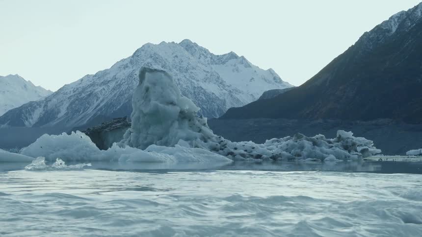 Water flows past an iceberg and mountain on a winter day