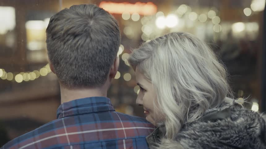 Woman looking amorously at a man while laying her head on his shoulder during an elevator ride where the man kisses her forehead