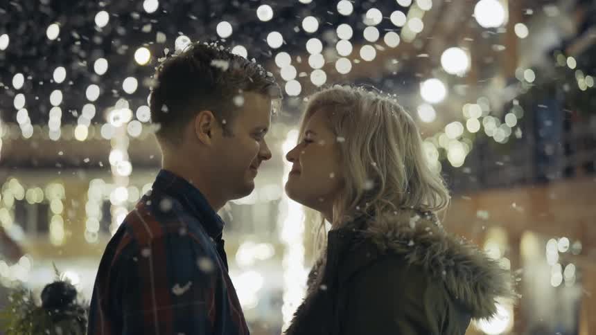 Man kissing a woman's forehead in a light snowfall