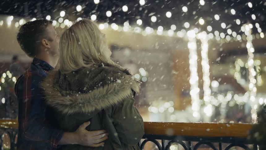 A man and woman watch snowflakes fall on a winter night