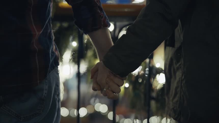 Man and woman hold hands in front of a fence