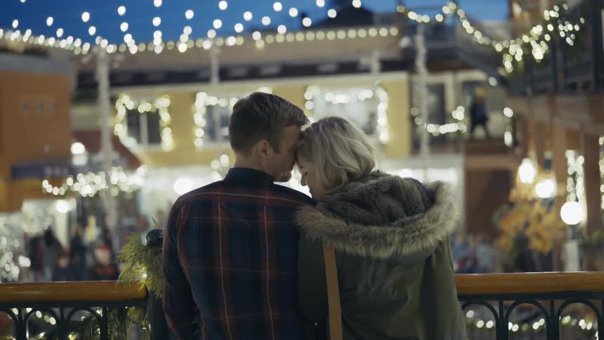 A male and female close to each other looking over a balcony at a shopping center