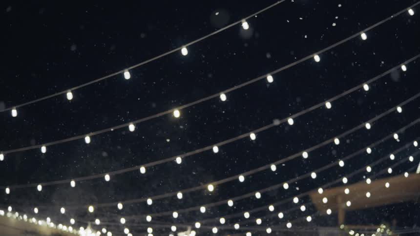 Snow falling down the sky during the night illuminated by small lights