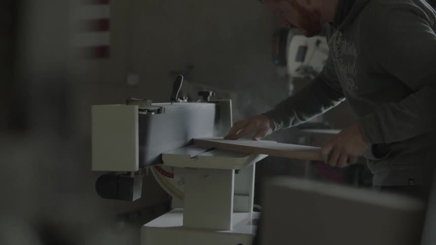 A bearded man sanding and shaping a piece of wood