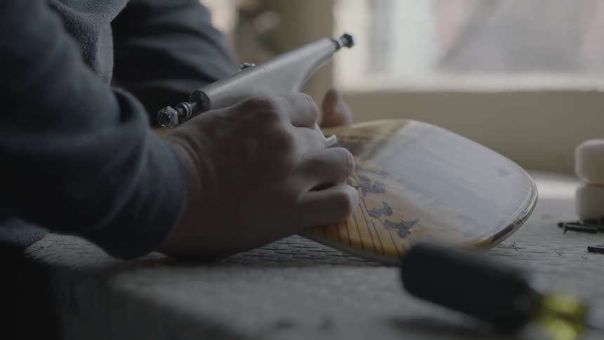 A man is putting a screw into his skateboard