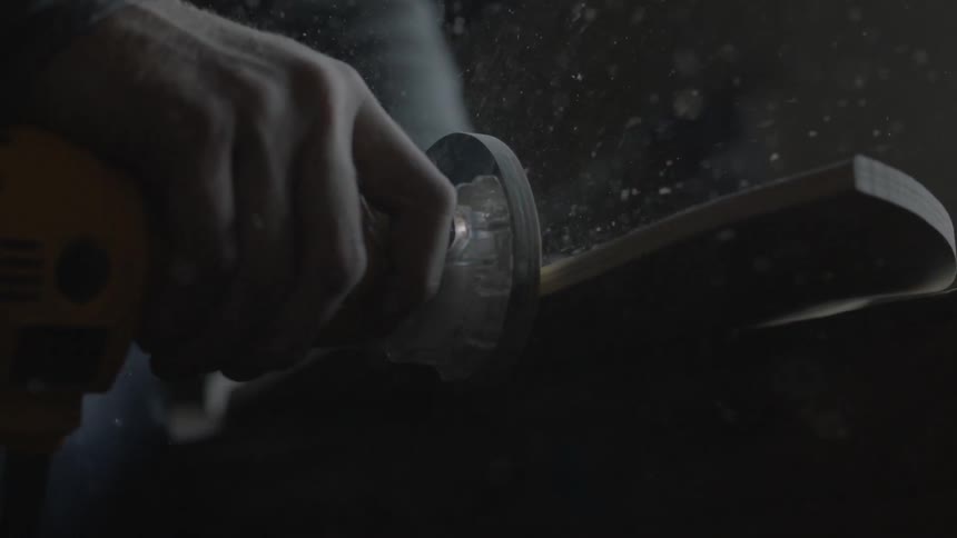 A man is grinding the side of a piece of wood