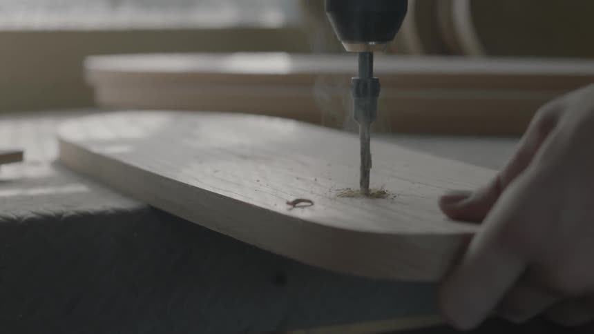 A drill is pressed through a wood board in a well light workshop