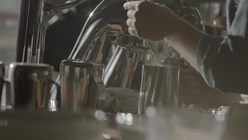 A barista fills a carafe with steaming hot milk