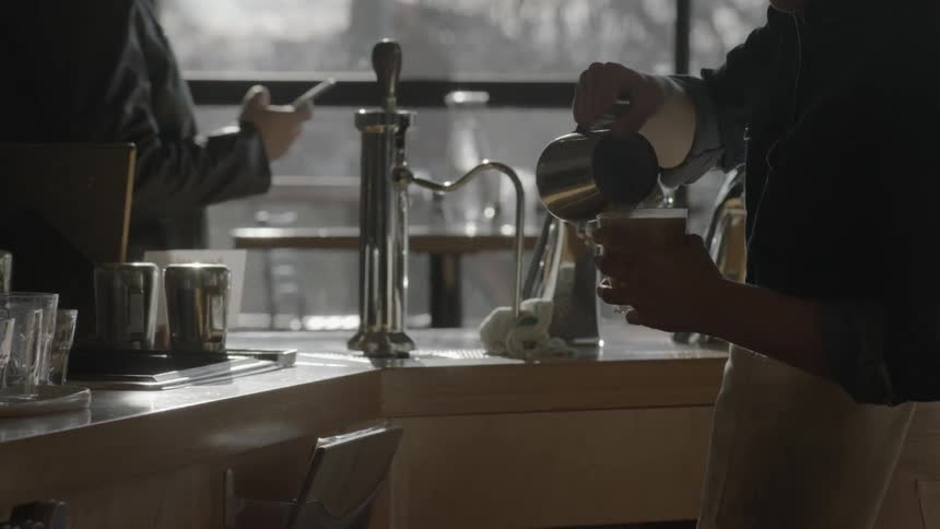 A barista pours steamed milk into a coffee and places it on a counter