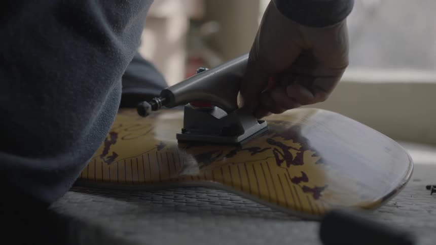 A man begins to put his skateboard together by hand