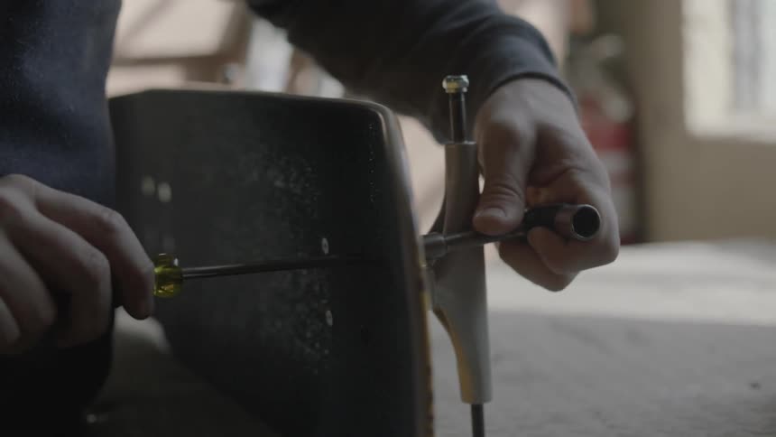 A man using a screwdriver to drive a screw through the deck of a skateboard