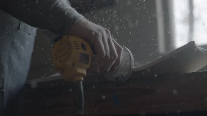 A man uses sander to smooth out the edges of a wooden board