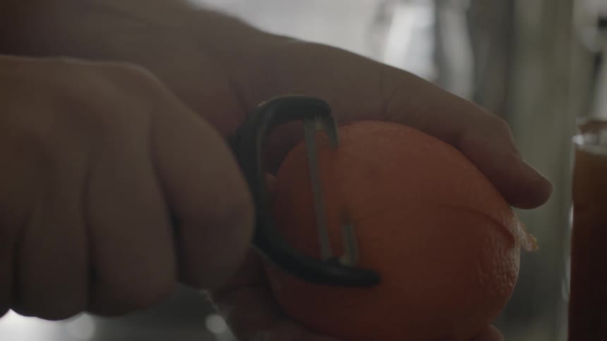 A man peels an orange with a peeler