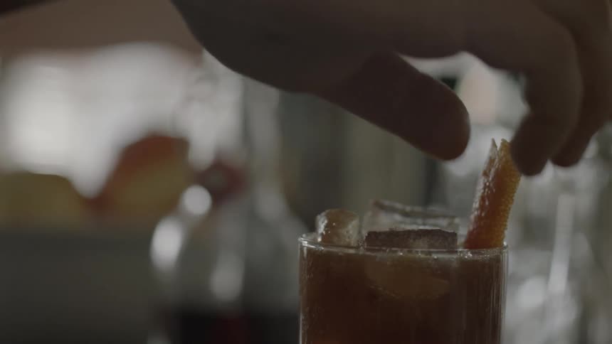 Someone garnishing an iced drink with orange peel