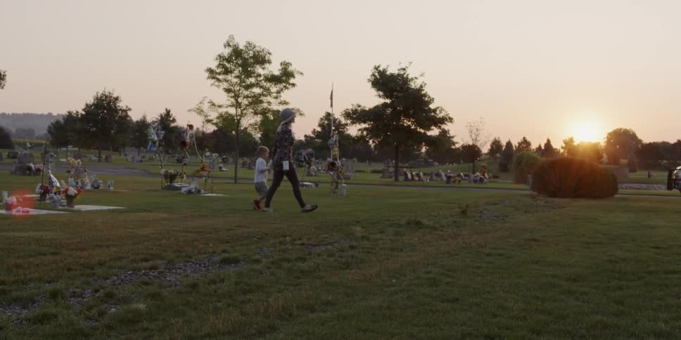 A woman leads a child by their hand through a cemetery in the sunset