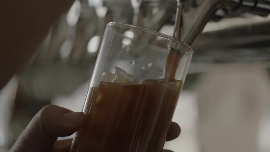 Liquid pours out of a spout and into a cup of ice