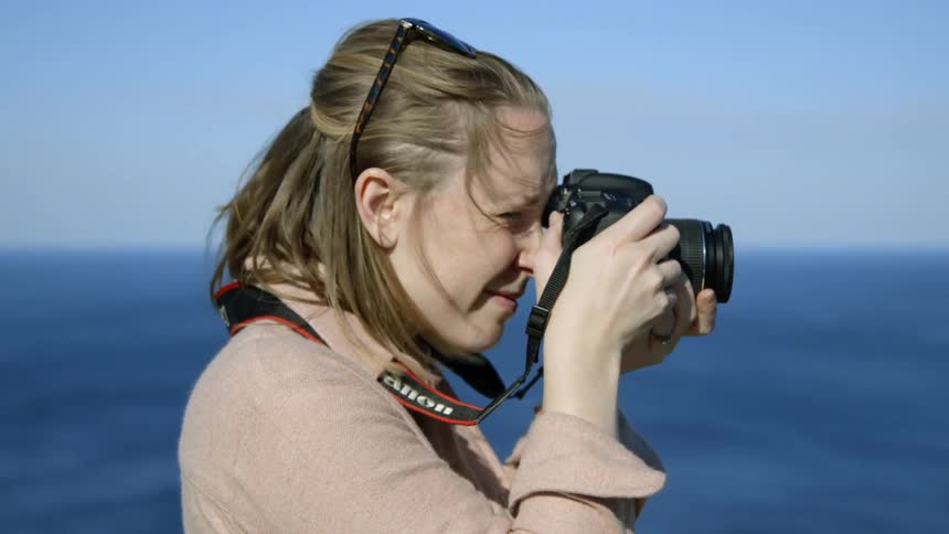Woman taking a picture with her camera next to a large body of water