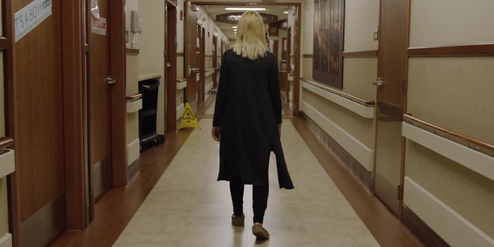 A female dressed in black slowly walking down a school hall being filmed from behind