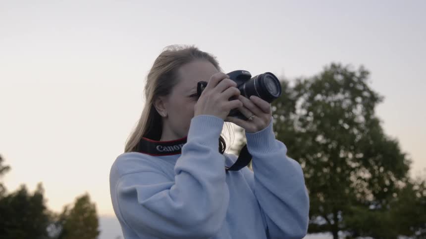 A woman looks through the viewfinder of a camera as she takes a shot and then inspects the result on the cameras display