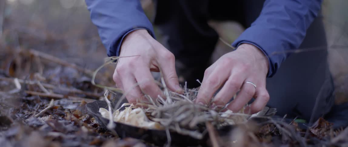 A person gathers a bundle of debris and twigs