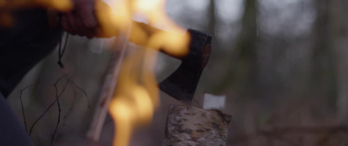 A man chops wood next to a fire