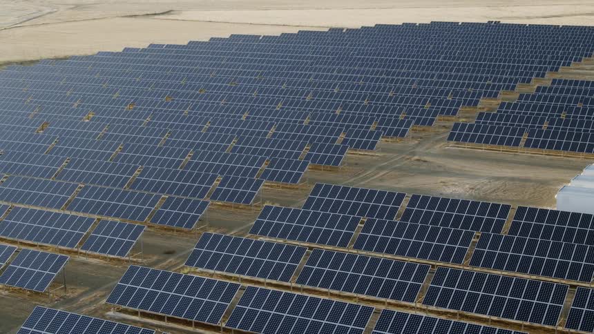 A solar farm sits in the desert with rows and rows of panels
