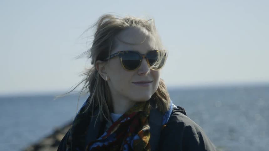 Woman smiling standing next to the sea and looking around her