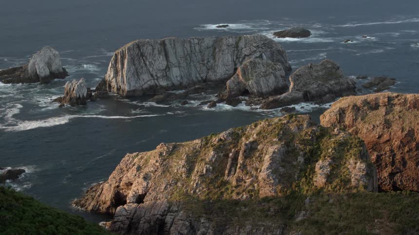 A large grassy mountain next to a calm sea