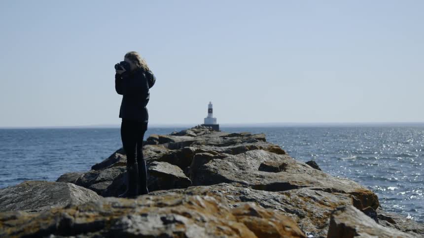 Woman standing on rocky pier taking a picture