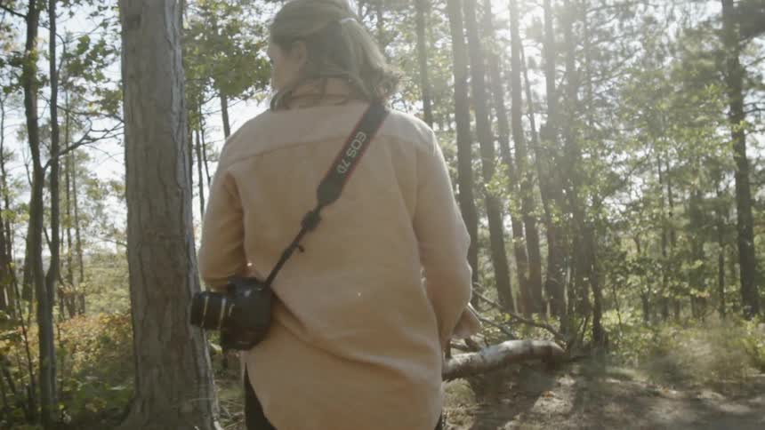 Woman walking through a forest with her camera hanging off her shoulder