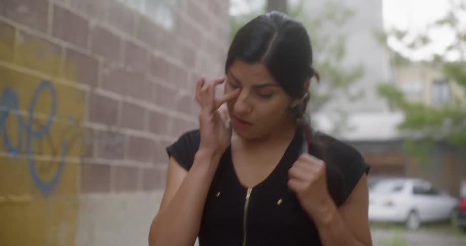 Woman walks through a puddle in an alleyway while wiping her eye