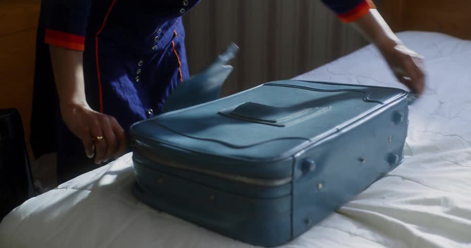 A young adult female opens a blue suitcase on top of a bed