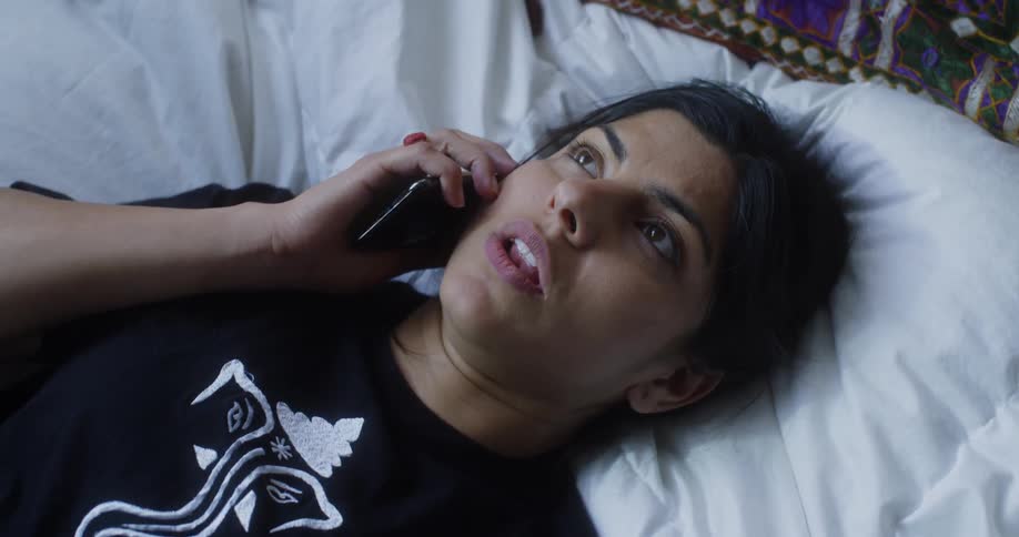 A woman lays in bed talking on her phone