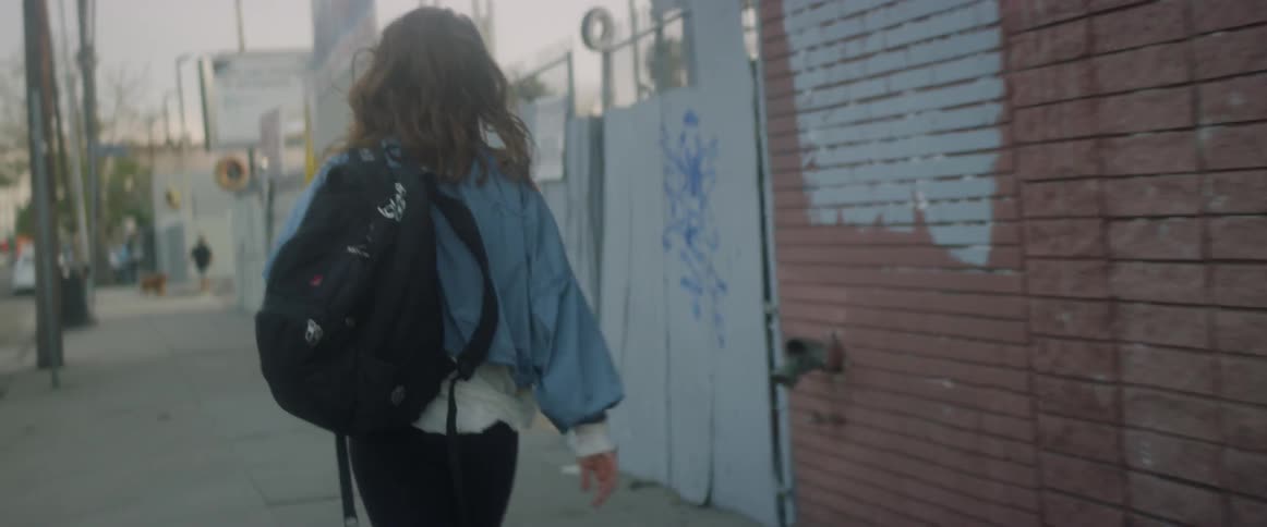 Young woman carrying a backpack walks down a city street