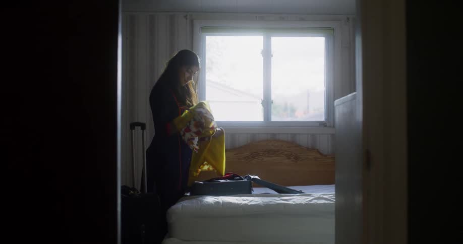 A woman takes a garment out of a suitcase and lays it on a bed