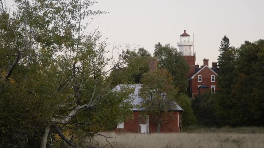A lighthouse with red bricks with trees around on a cloudy day